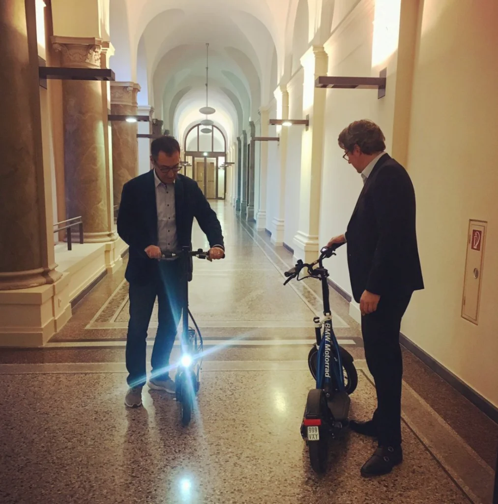Cem Özdimir und Andreas Scheuer fahren auf dem Flur des BMVI E Scooter
